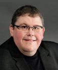 Headshot: Man in dark shirt with glasses smiling at camera